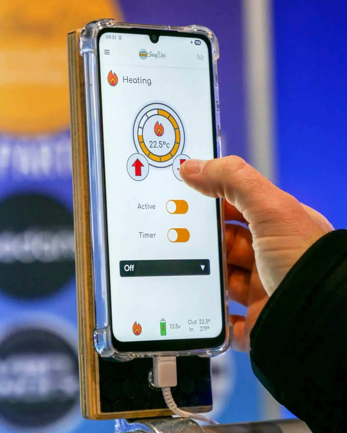 A hand using the heating screen of the SavvyVan phone app, set to 22.5°C, on a phone mounted at the SavvyVan stand