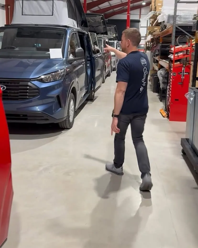 One of the SavvyVan team walking past campervans in a conversion workshop