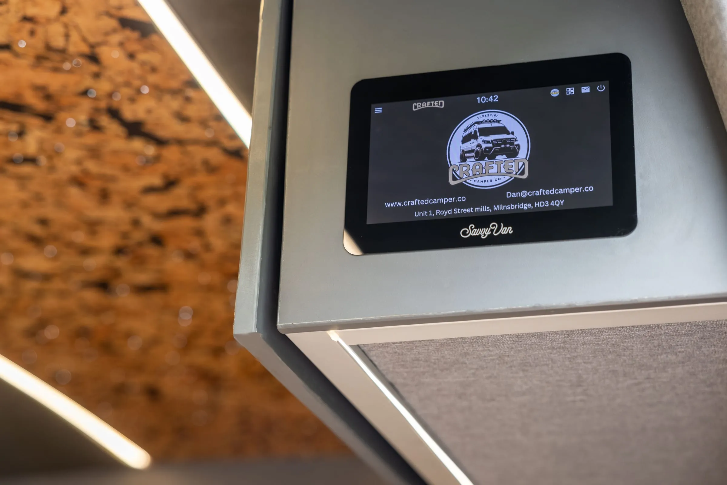 A SavvyVan panel fitted in a finished conversion, its screen showing Crafted Camper Co’s logo, website, email address and workshop address