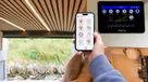 A hand holding a phone showing the SavvyVan app's switching screen, with a SavvyVan3 panel fitted in the van behind it