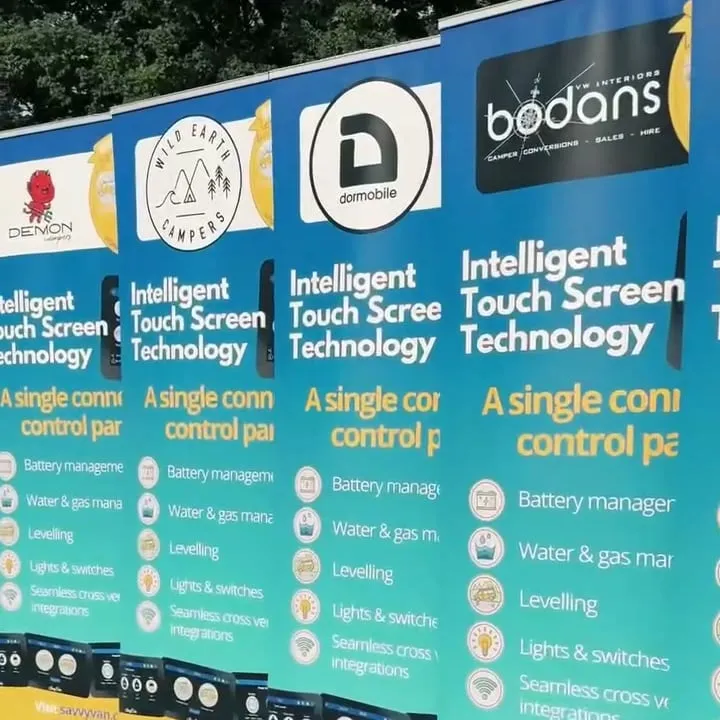 A row of pull-up banners on the grass, each carrying a converter’s logo above a list of what the SavvyVan panel does