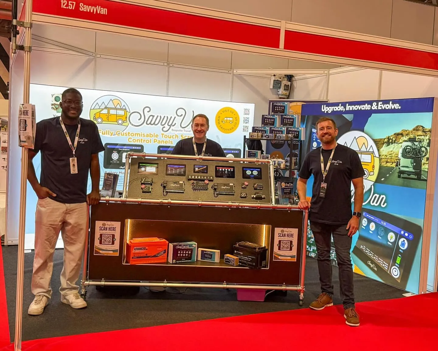 Parbi, Simon and Greg on SavvyVan stand 12.57 at the NEC in October 2025, around a demonstration board of SavvyVan panels and modules