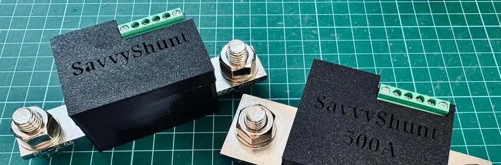 The 300A and 500A SavvyShunt models on a cutting mat, each a black module on a metal shunt bar with heavy copper terminals